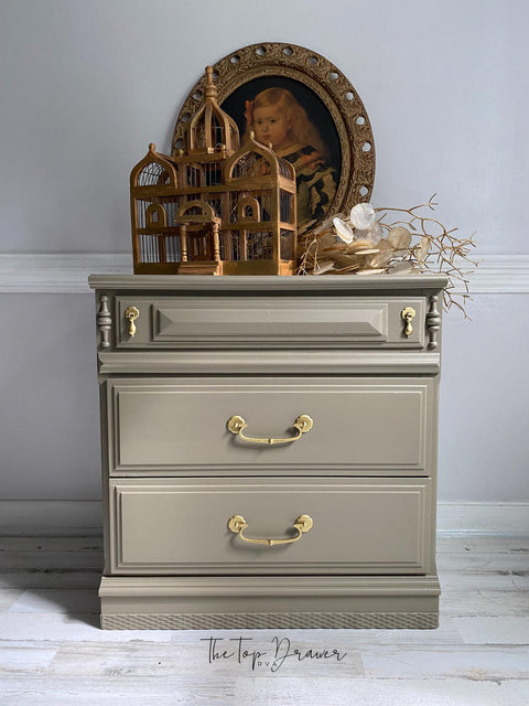 WoodUBend Trim #TR716 (Set of 2) is the perfect mouldable embellishment for any project!  A brown chalk painted night stand with gold handles.  WoodUbend is applied to the bottom front of the night stand.  The night stand is staged on a whitewashed wood floor, in front of a gray wall with white wood trim.  A brown wooden bird nest, brown branches and an oval picture of a young girl sit on top of the night stand.
